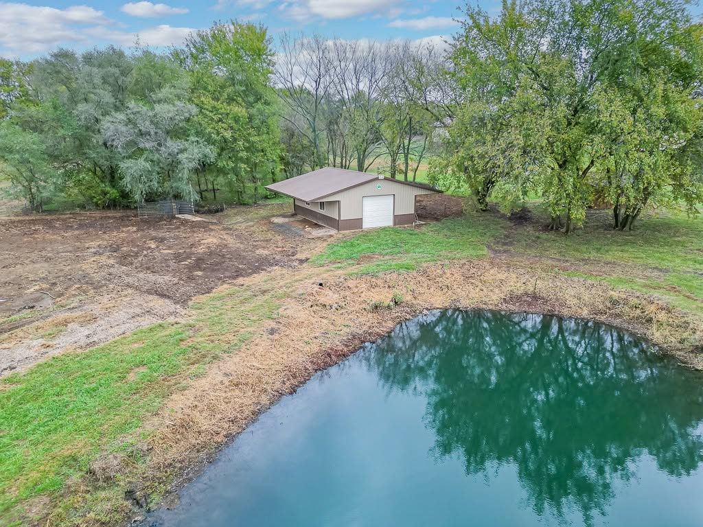 Rural property with pond, metal barn structure, and mature trees on grassy land