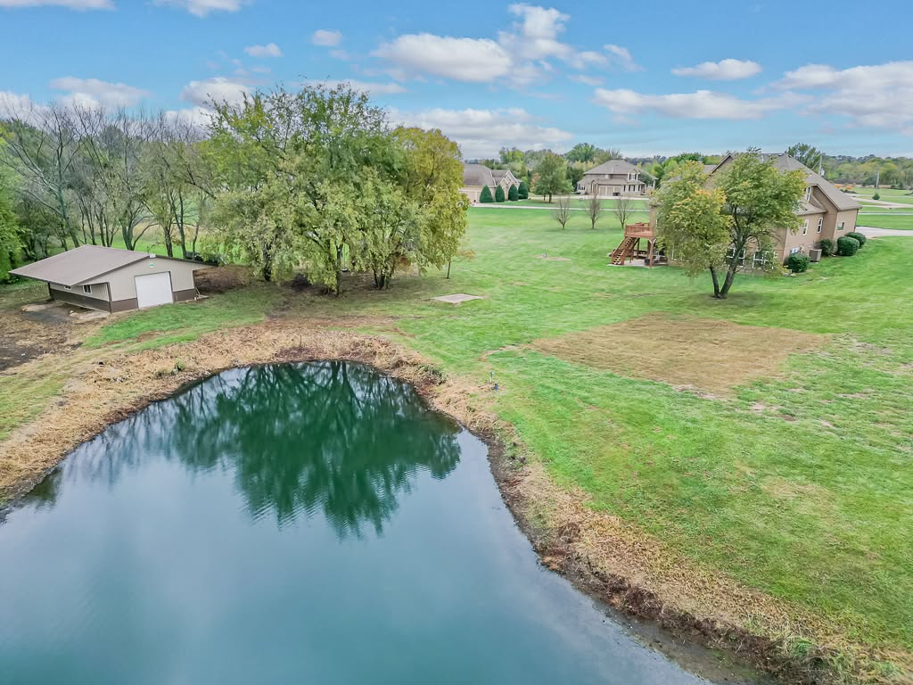 Aerial view of rural property with pond, barn, and residential homes on green acreage