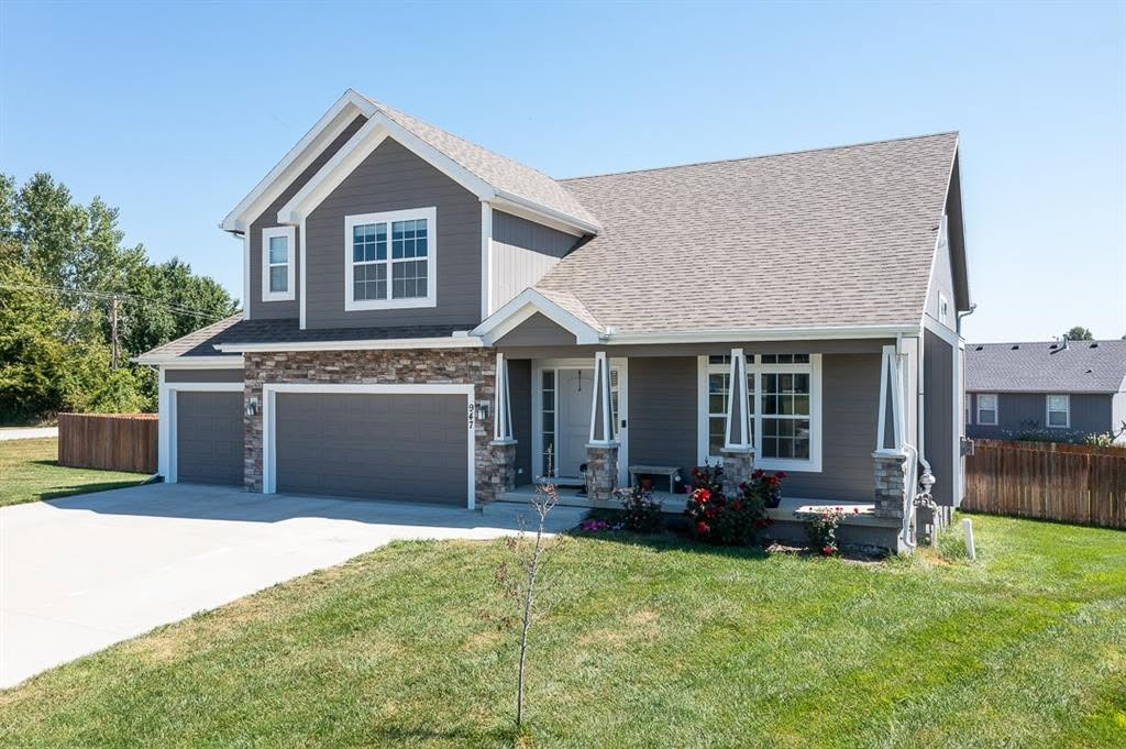 Two-story gray and white house with stone accents, two-car garage, and front porch