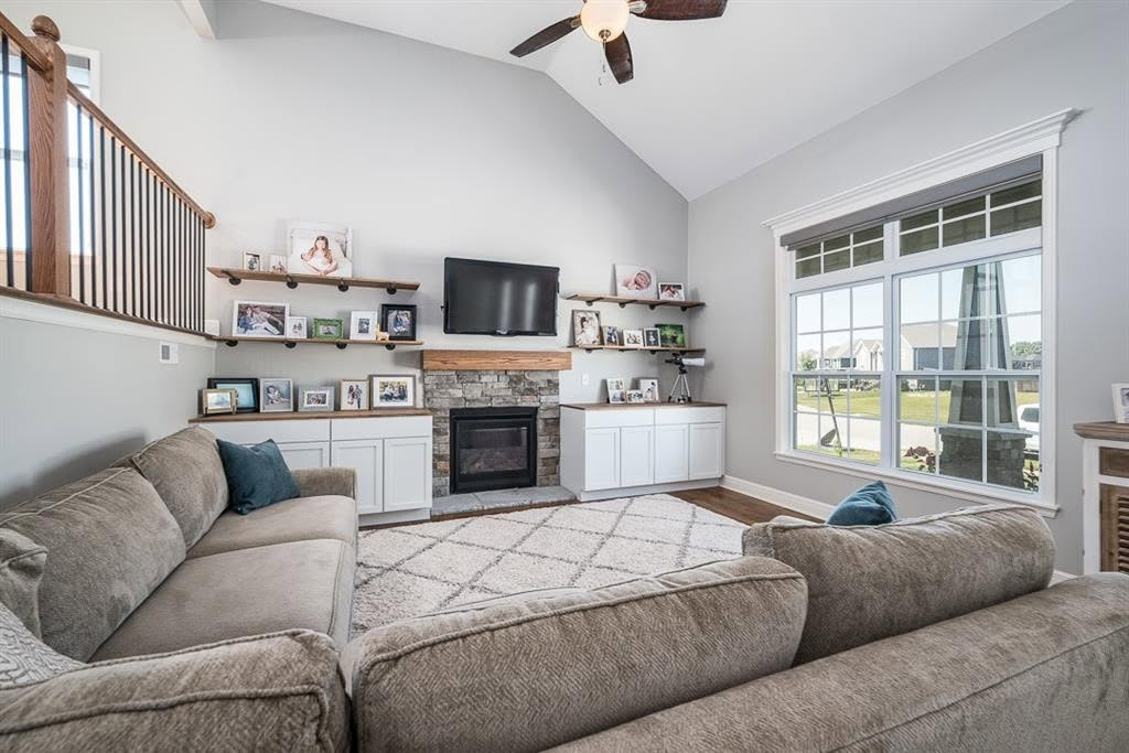 Modern living room with gray sectional sofa, fireplace, white cabinetry, and large windows overlooking landscape