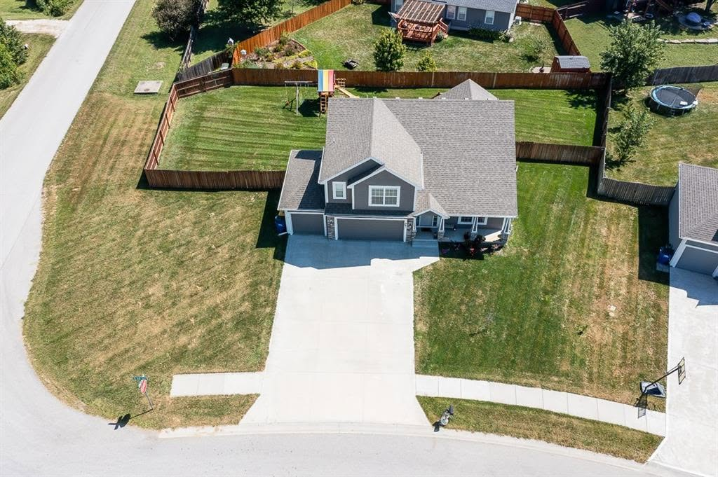 Aerial view of two-story gray house with driveway and fenced yard in residential neighborhood