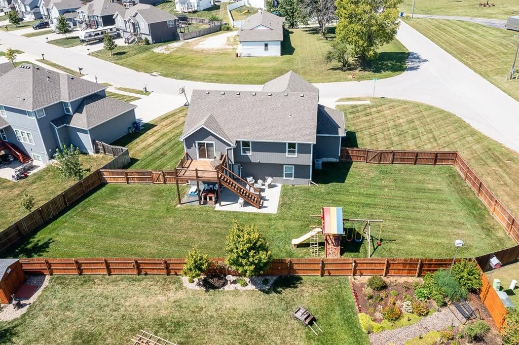 Aerial view of two-story gray house with wooden deck, fenced backyard, and landscaping