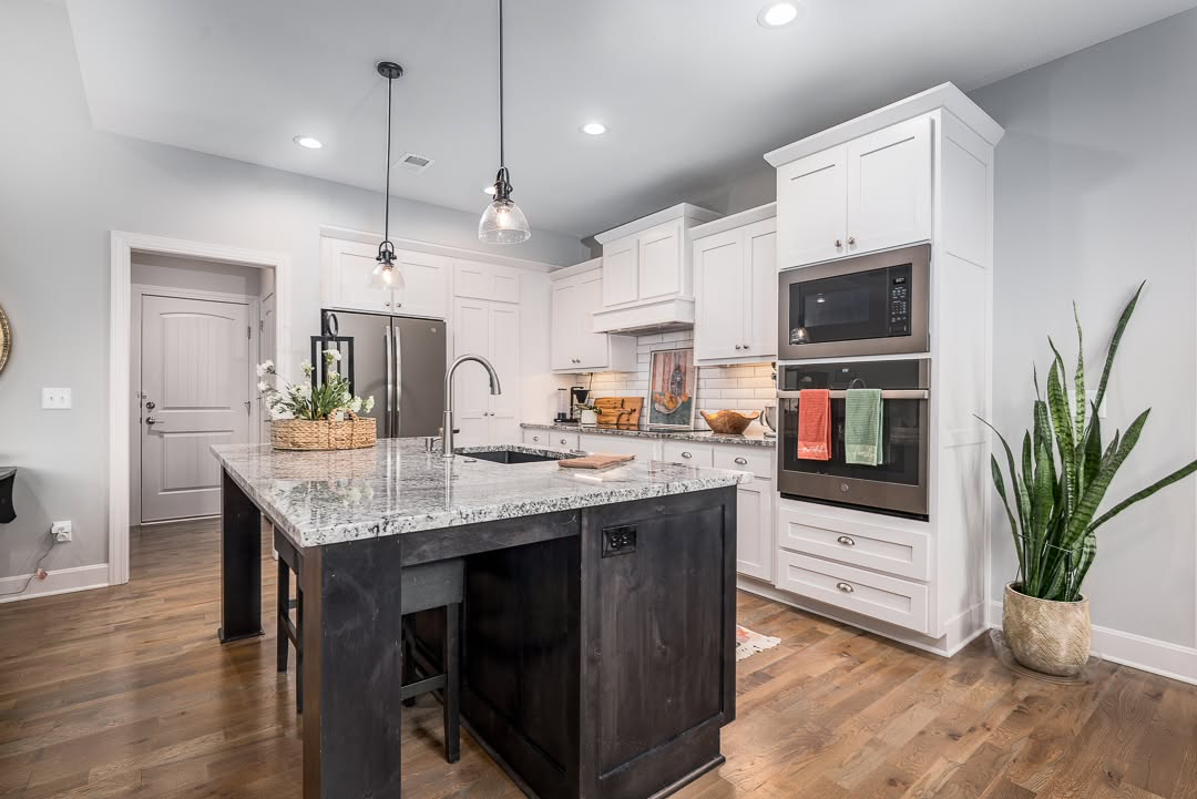 Modern kitchen with white cabinetry, dark island, granite countertops, and stainless steel appliances