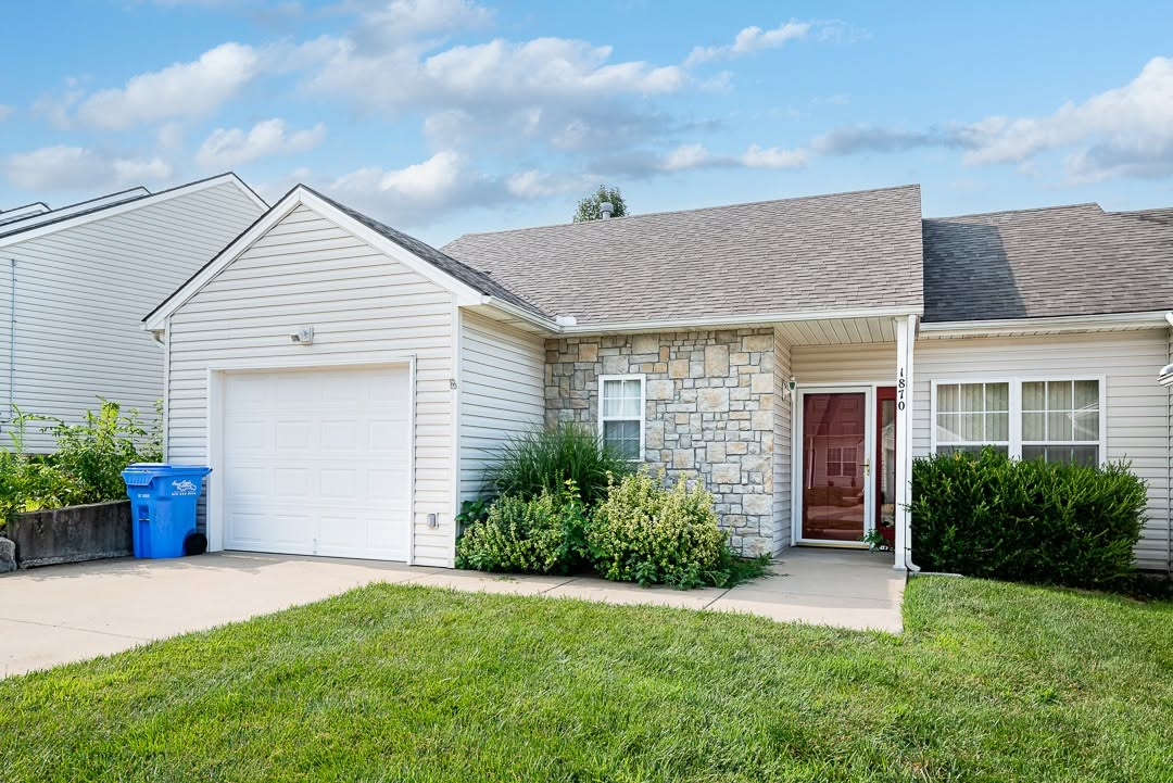 Single-story suburban home with white siding, stone accent wall, red door, and attached garage