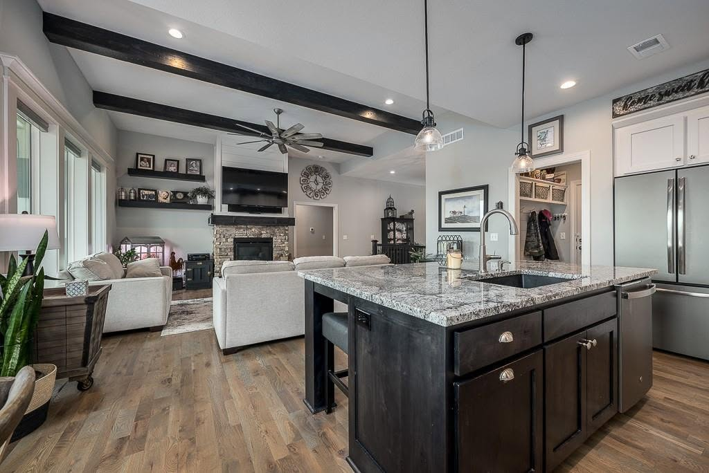 Modern open-concept kitchen and living room with granite island, stainless steel appliances, and black exposed beams