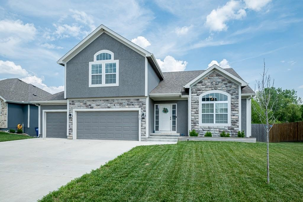Modern two-story home with stone and blue siding, three-car garage, and manicured lawn