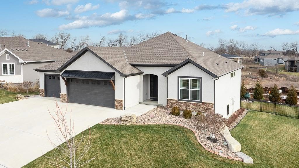 Modern white house with dark trim, stone accents, two-car garage, and landscaped front yard